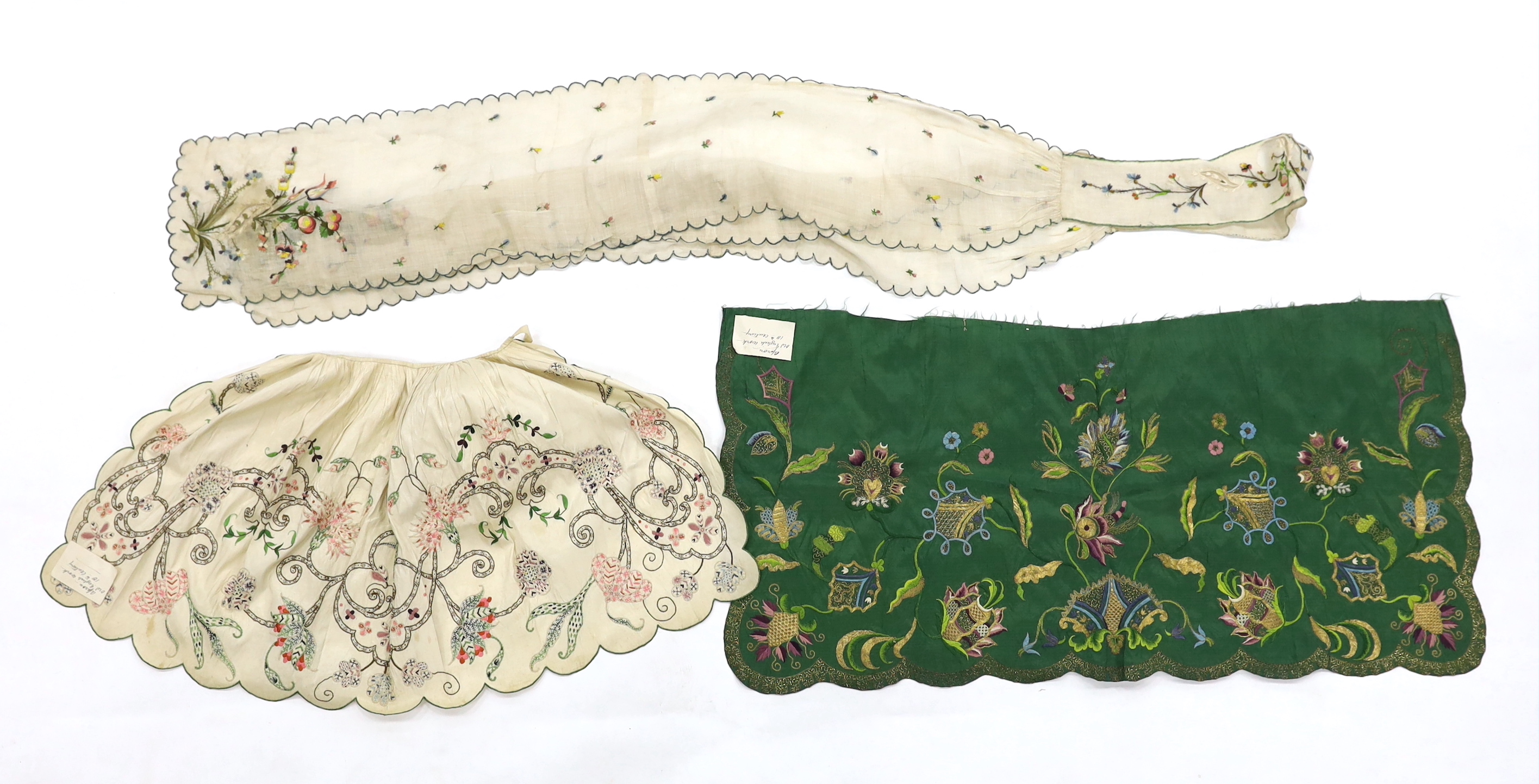 A late 18th century green silk scalloped bordered lady’s apron border, ornately embroidered with gold metallic threads and polychrome silk, in a large vine, floral and leaf design, together with a similar cream silk embr